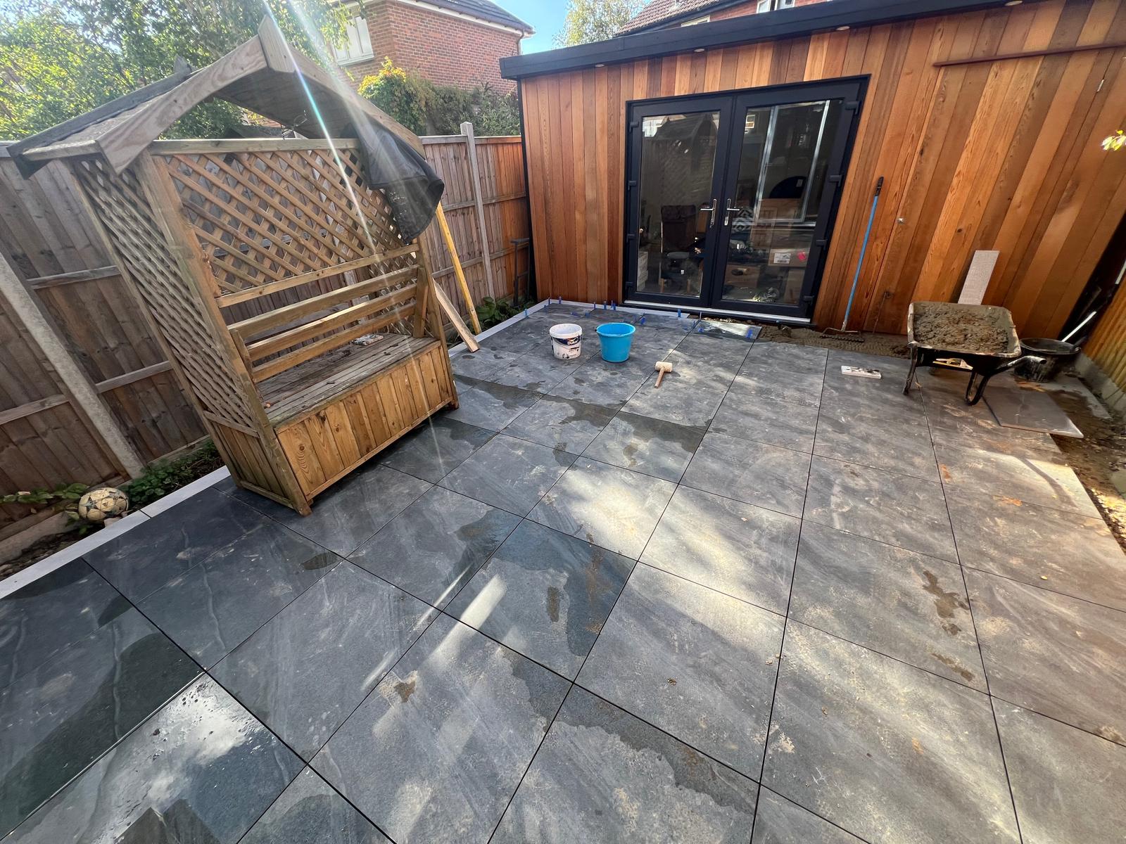 Grey porcelain patio installation in progress beside a garden studio