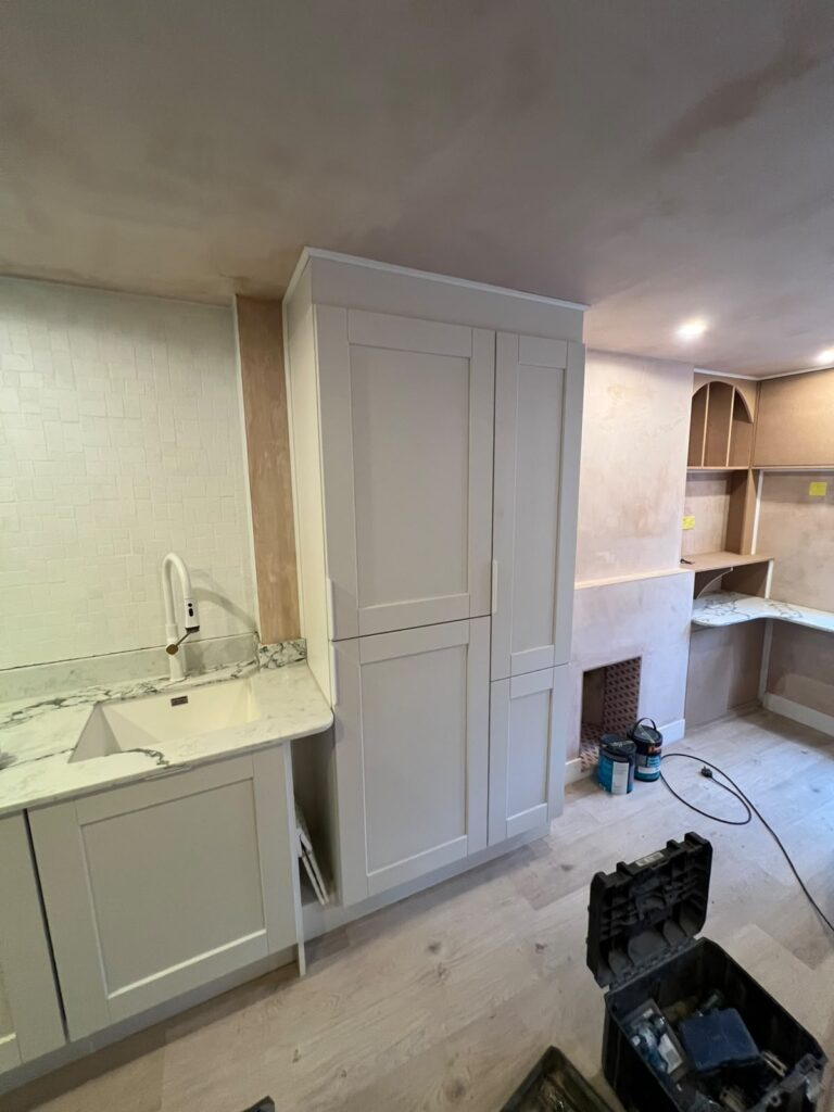 Shaker-style tall larder cupboards beside a sink with marble-effect worktop